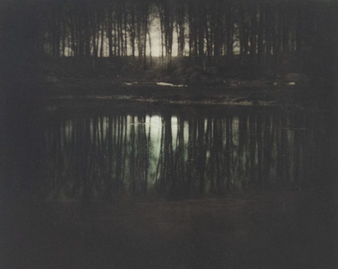 A photograph of a moonrise with trees reflecting in water.