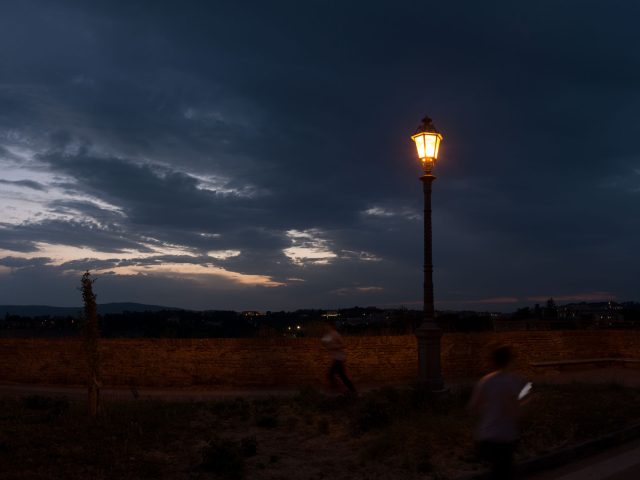 This is a color photograph of a man running past a lamp post at night.