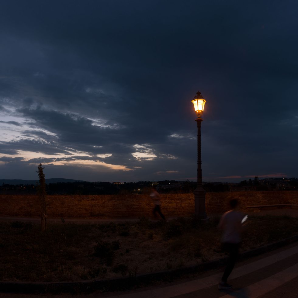 This is a color photograph of a man running past a lamp post at night.