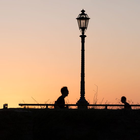 This is a color photograph of two people walking past a lamp post at sunset.