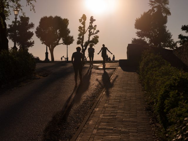 This is a color photograph of a group of people walking towards the sun as it sets.