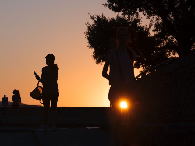 This is a color photograph of some one walking during sunset.