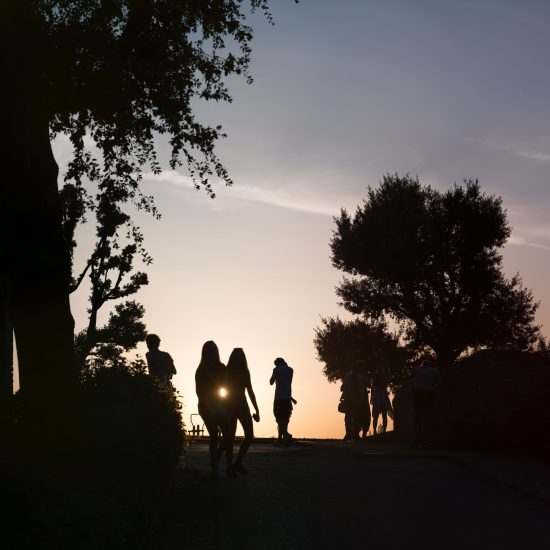 This is a color photograph of people walking in a park as the sun sets.
