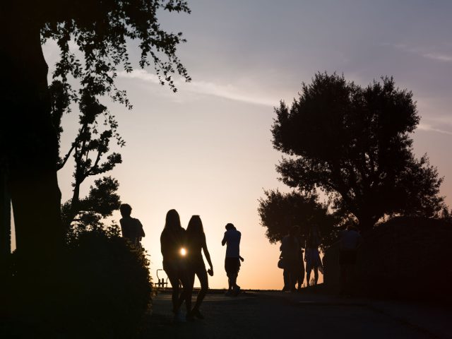 This is a color photograph of people walking in a park as the sun sets.