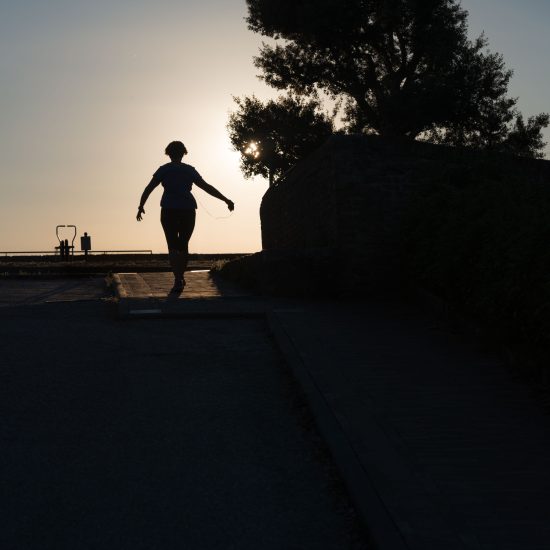 This is a color photograph of a person running towards the sunset.