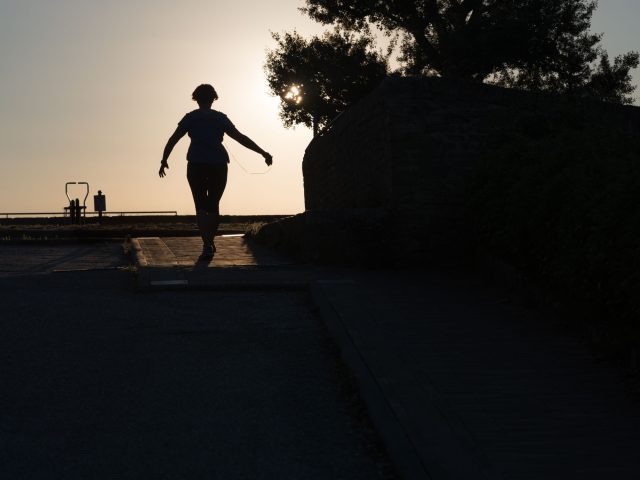This is a color photograph of a person running towards the sunset.
