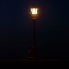 This is a photograph of a lamp post at night as someone walks by.