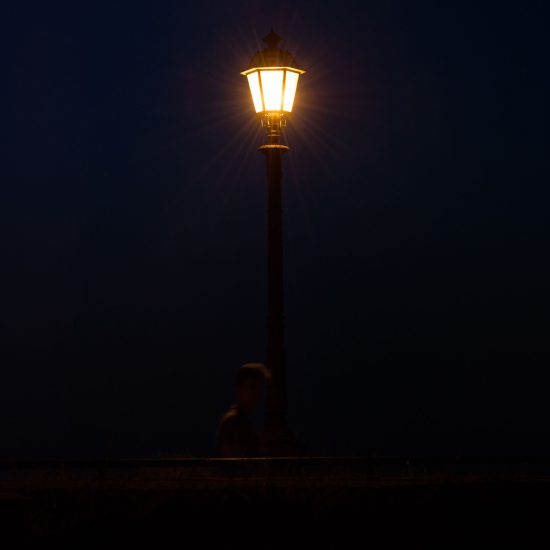 This is a photograph of a lamp post at night as someone walks by.