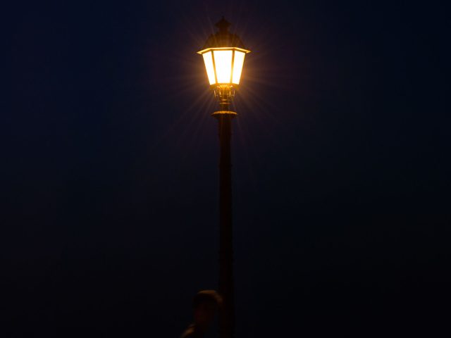 This is a photograph of a lamp post at night as someone walks by.