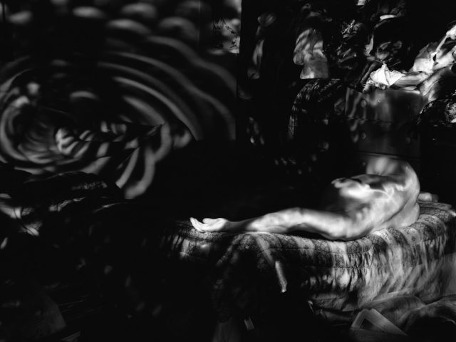 Tis black and white photograph shows ghostly figures sprawled across a bed. Circles of light are cast on the bedroom walls.
