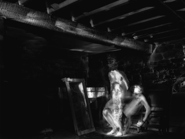 A black-and-white photograph of two ghostly figures in a darkened space.