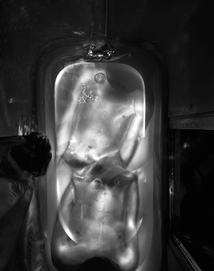 This is a black and white photograph of a mans torso in the bathtub mirrored on both sides.