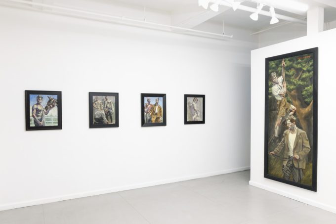 This image shows the white walls of a gallery, where a large vertical paintining by Mark Beard depicts men climbing trees. Behind them, four smaller paintings of men hang.