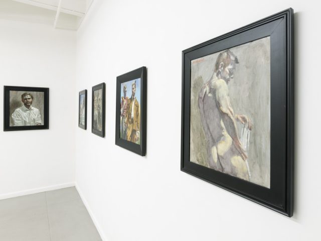 This photograph shows the walls of a gallery where five framed paintings hang. They depict men performing various activities.