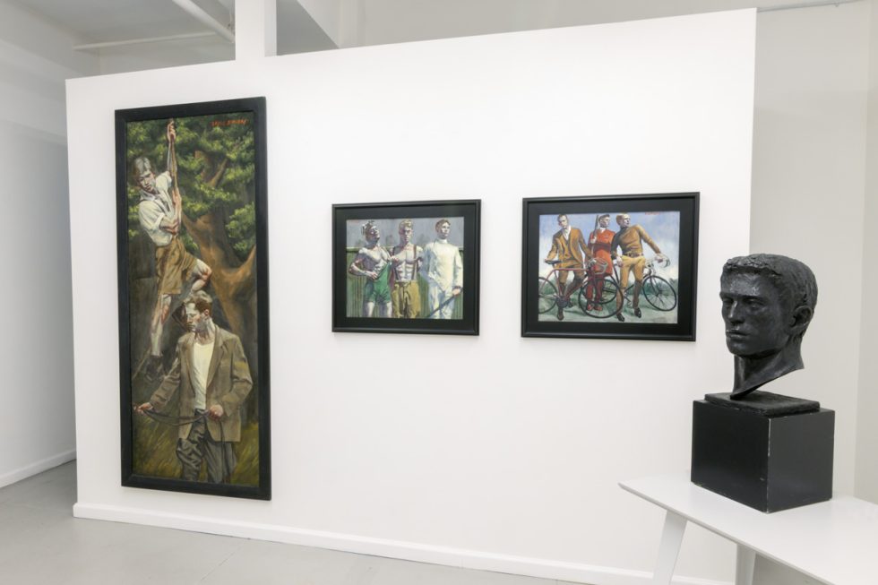 This photograph shows the walls of the gallery space where three framed paintings hang. On a table in the foreground, stands a black statue of a man's head from the neck up.