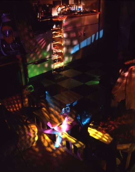 This color photograph shows a kitchen, mostly dark, but lit with scattered rainbows cast across the floor.