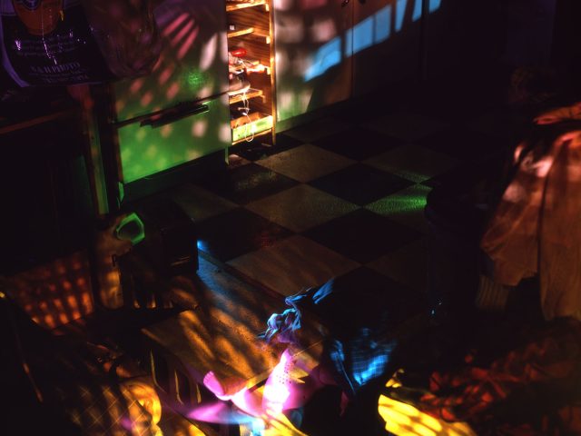 This color photograph shows a kitchen, mostly dark, but lit with scattered rainbows cast across the floor.