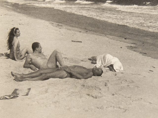 In this image, four figures are lounging on the sands of a beach.