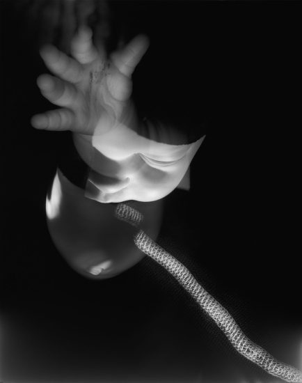 This black and white image shows a ghostly hand reaching outwards. A thick chord snakes upwards.