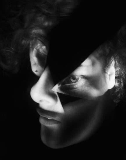 This vertical black and white photograph shows the face of. man whose features are contorted and altered in size.