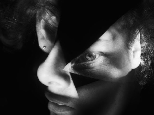 This vertical black and white photograph shows the face of. man whose features are contorted and altered in size.