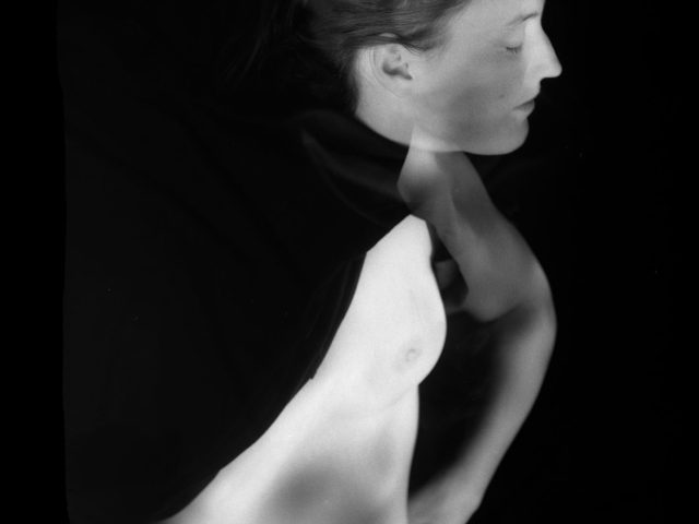 This black and white image shows the faint body of a woman, facing off to the right as if headed in that direction.