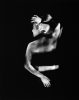 This black and white photograph shows the back of a woman who reached behind herself with what seems like more than two arms. Her limbs are blurred with motion.