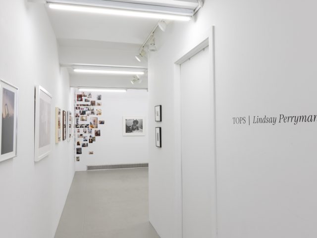 This photograph shows a gallery space with the title of the exhibition, Tops. Photographs are visible in the back room.