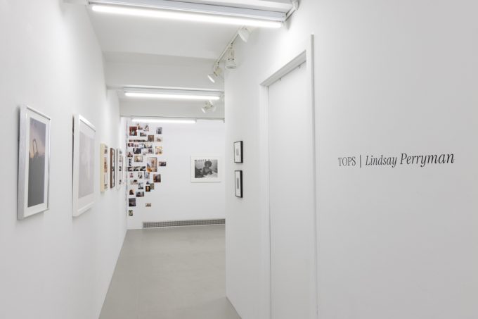 This photograph shows a gallery space with the title of the exhibition, Tops. Photographs are visible in the back room.