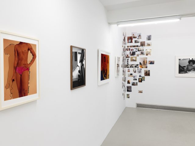 This image shows the walls of a gallery space covered in a collage and framed photographs by an artist named Lindsay Perryman.
