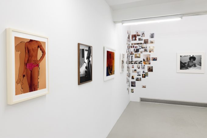 This image shows the walls of a gallery space covered in a collage and framed photographs by an artist named Lindsay Perryman.