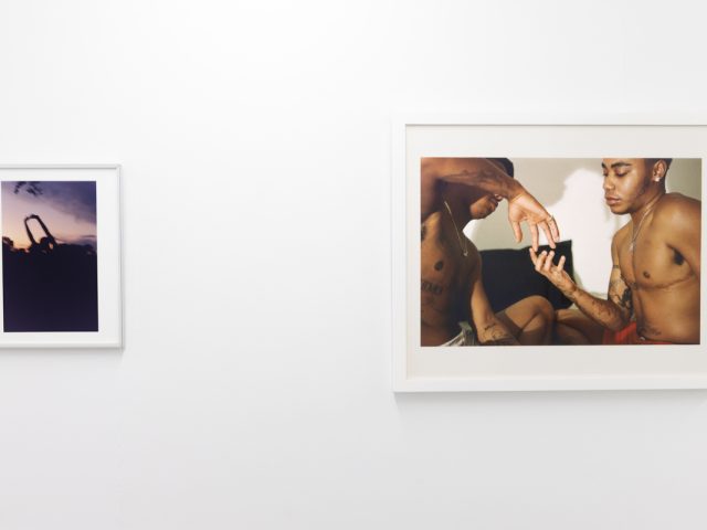 This image shows the walls of a gallery where two framed photographs by an artist named Lindsay Perryman hang.