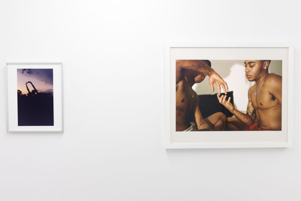 This image shows the walls of a gallery where two framed photographs by an artist named Lindsay Perryman hang.