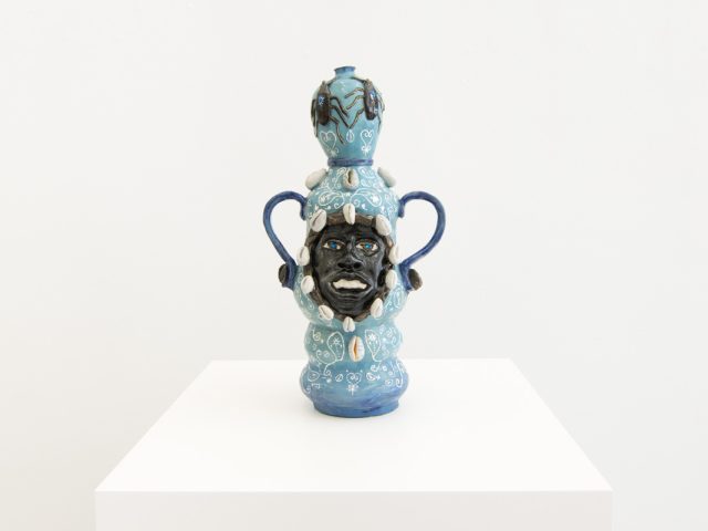 This image shows a ceramic sculpture with the face of a man inlayed. It is multiple shades of blue with white details.