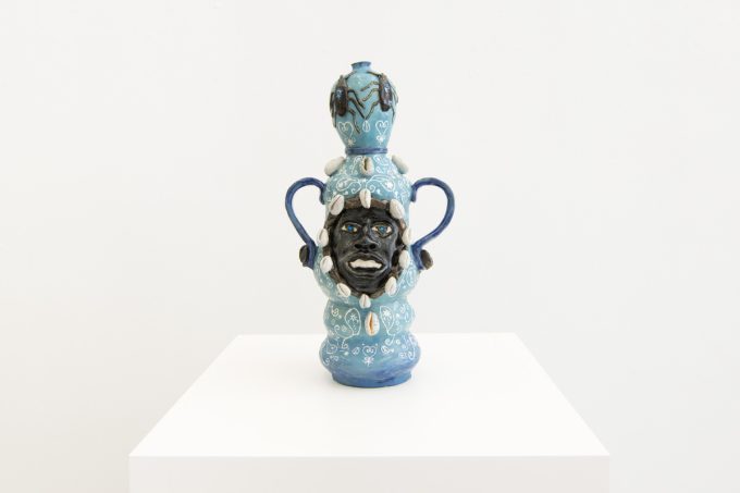 This image shows a ceramic sculpture with the face of a man inlayed. It is multiple shades of blue with white details.