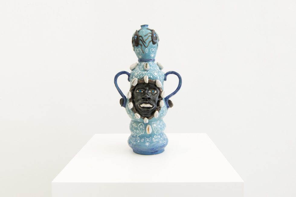 This image shows a ceramic sculpture with the face of a man inlayed. It is multiple shades of blue with white details.