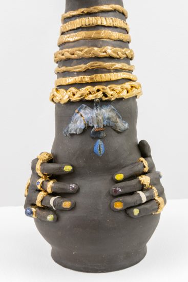 This image shows a ceramic sculpture close up. Its hands are adorned with multi-colored rings.