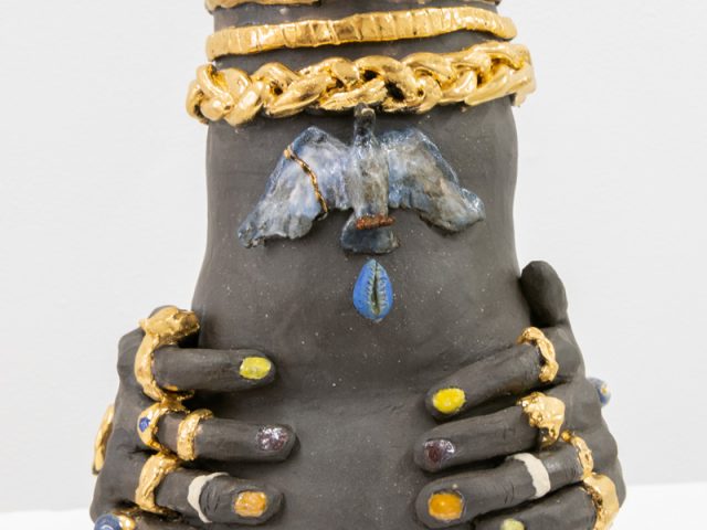 This image shows a ceramic sculpture close up. Its hands are adorned with multi-colored rings.
