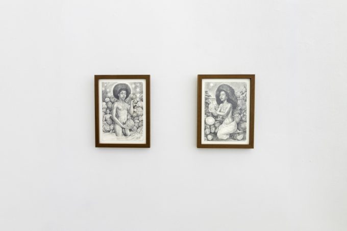 This photo shows two black and white drawings of women in nature hanging on a white wall.