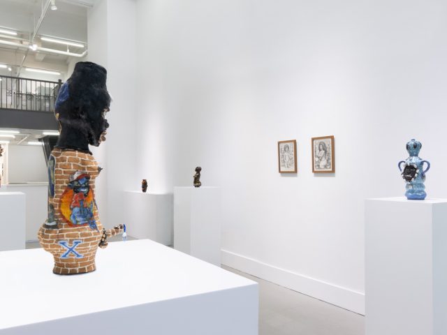 This image shows the back of a ceramic sculpture facing a room full of other sculptures and drawings.