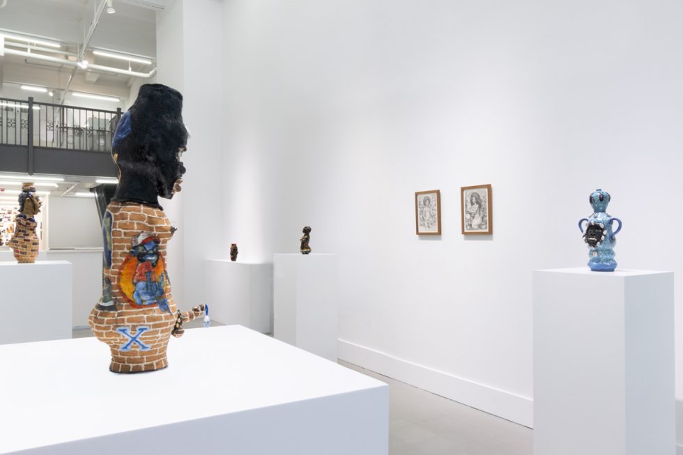 This image shows the back of a ceramic sculpture facing a room full of other sculptures and drawings.