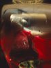 This color photograph shows a blurred, enlarged face. It is partially obscured by a strange mirror-like object, with the top petals of a red rose underneath.