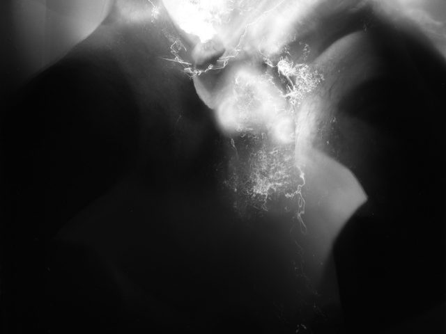 This black and white photograph shows the naked body of a man plunged into water that reflects light brightly.