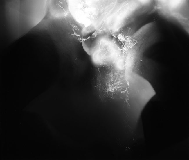 This black and white photograph shows the naked body of a man plunged into water that reflects light brightly.