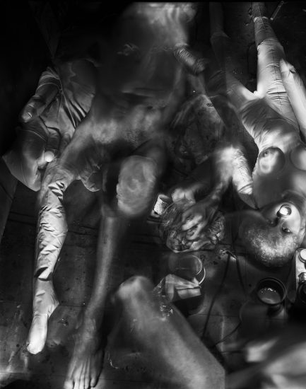 This photograph shows the crowded floor of an apartment where naked bodies and dolls are strewn across the ground.