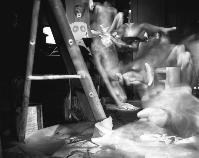 This black an. white photograph shows the naked bodies of men layered overtop of one another in an apartment.