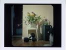 In this image, a vase of yellow and purple flowers sits on a white table above a pair of free weights.