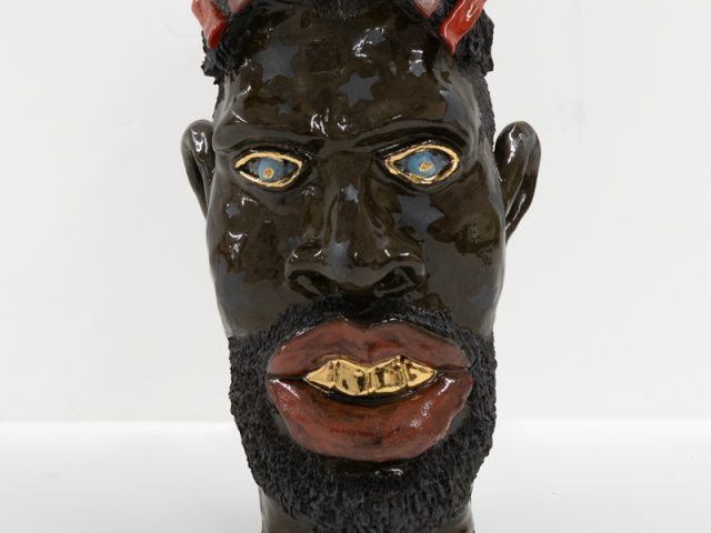A ceramic vessel with dark brown glazing depicting a man's head.