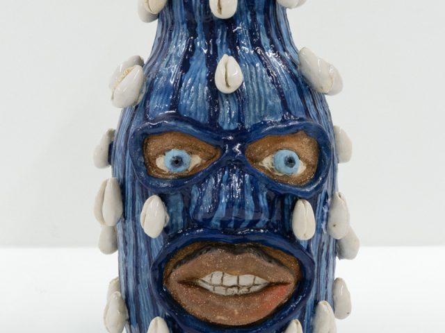 This is a small ceramic sculpture painted with dark and light blue stripes. Small shells rise from its sides.