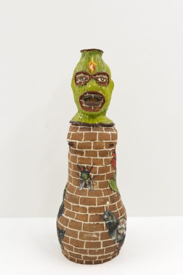 A ceramic vessel depicting a figure with a green hood and a brick body.